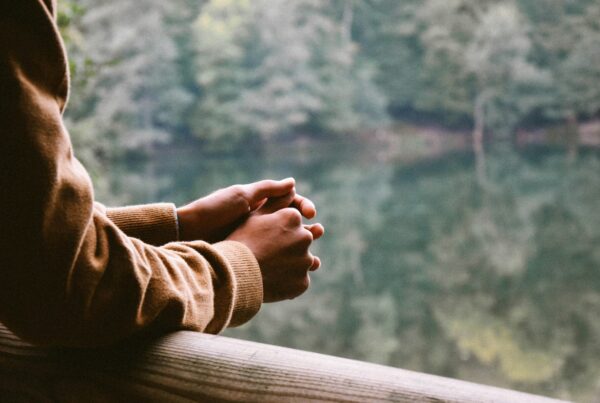 Persona con las manos entrelazadas en actitud pensativa frente a un paisaje natural, simbolizando reflexión y estrés emocional.