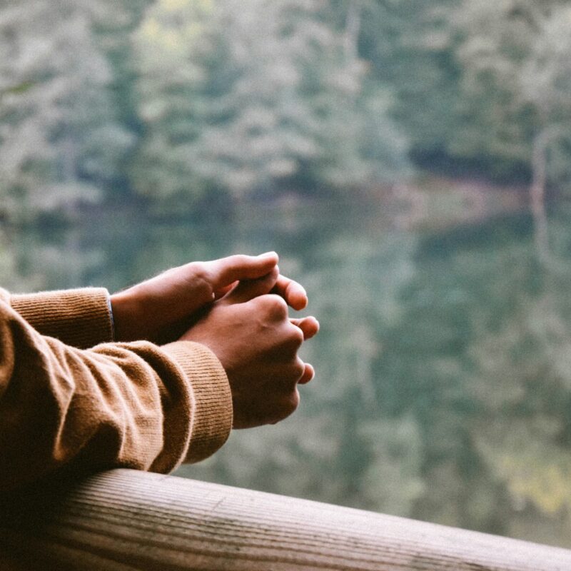 Persona con las manos entrelazadas en actitud pensativa frente a un paisaje natural, simbolizando reflexión y estrés emocional.