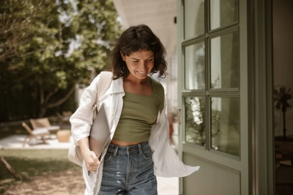 Mujer joven saliendo activa de casa con su portátil, simbolizando la agilidad de realizarse una analítica operatoria