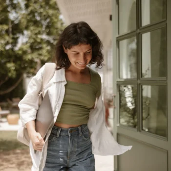 Mujer joven saliendo activa de casa con su portátil, simbolizando la agilidad de realizarse una analítica operatoria